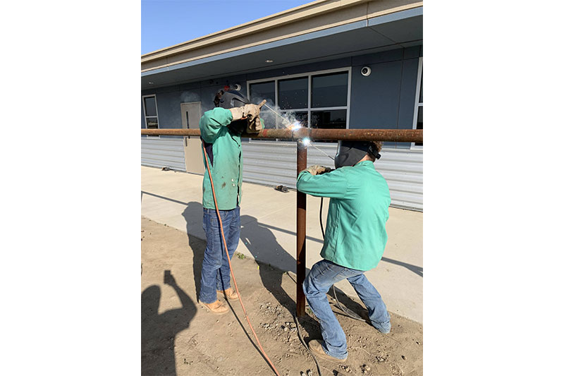 Two students welding the metal fence post